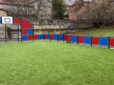 Pista multideporte instalada con paneles rojos y azules, canastas y porterías y con césped artificial