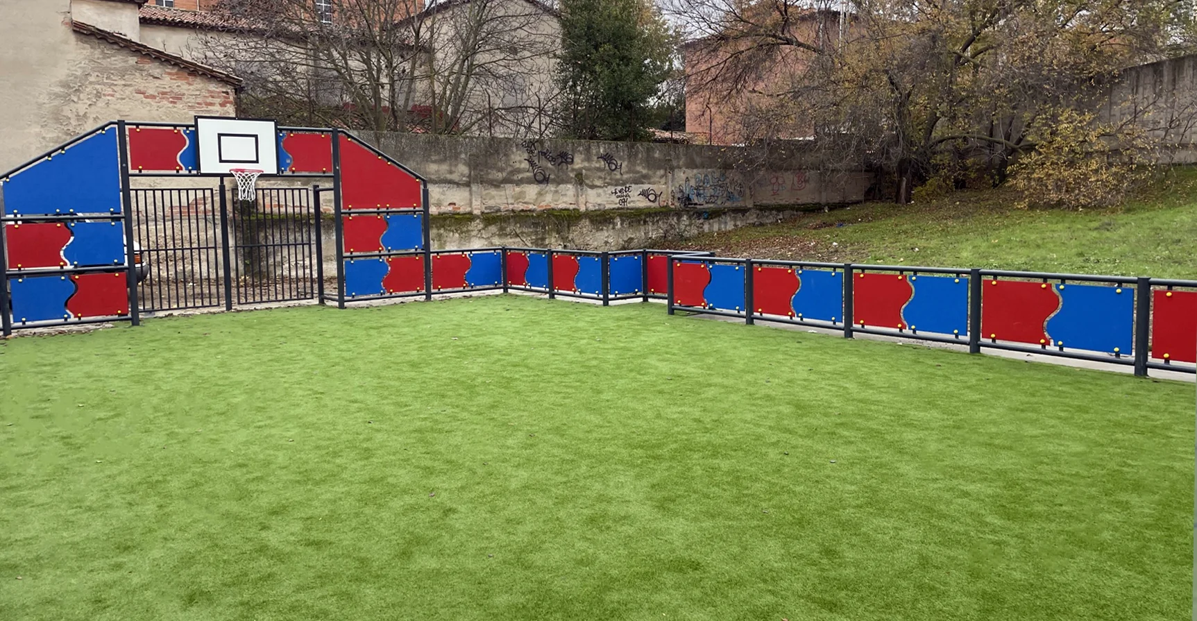 Pista multideporte instalada con paneles rojos y azules, canastas y porterías y con césped artificial