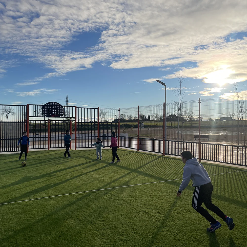 Imagen de niños jugando con un balón en una pista multideporte antes de la caída del sol