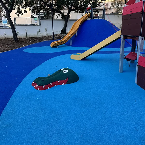 Parque infantil instalado sobre pavimento continuo color azul con cabeza de un cocodrilo sobresaliendo
