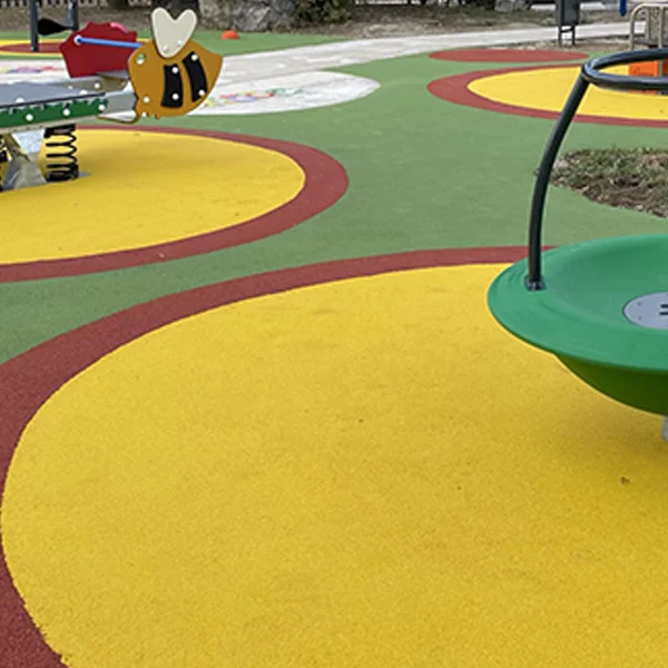 Parque infantil con pavimento continuo de caucho en tonos verdes, amarillos y rojos